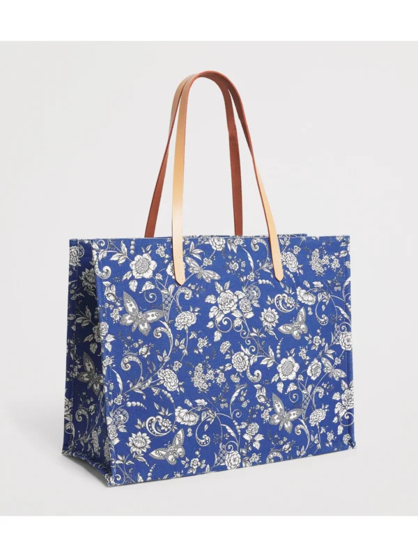 HARRODS Large Cotton Butterfly Tote Bag_3 Harrods 藍色女用托特包印花細節特寫,布滿精緻花朵與蝴蝶,並點綴經典金色 Harrods 字母商標