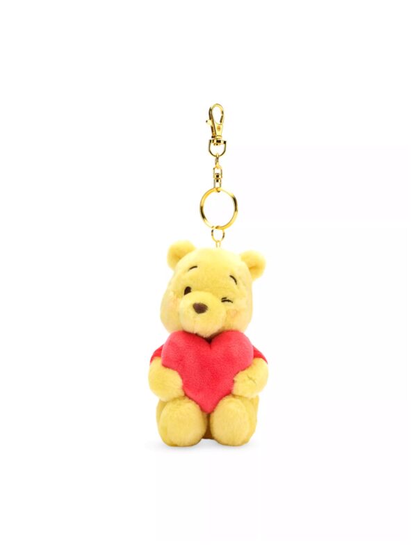 DNAK2610001-36-scaled-uni 英國 Disney 小熊維尼黃色絨毛包包吊飾正面,雙手抱紅色天鵝絨愛心,臉頰有紅暈刺繡細節
