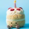 JCDB2630003-82_4 JELLYCAT 生日蛋糕絨毛玩偶放置於木質桌面,展現居家擺設風格